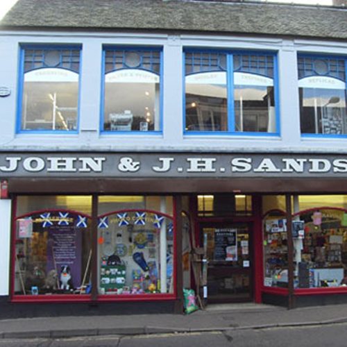 A shop front with very large windows with red frames displaying miscellaneous objects underneath large windows with blue frames.
