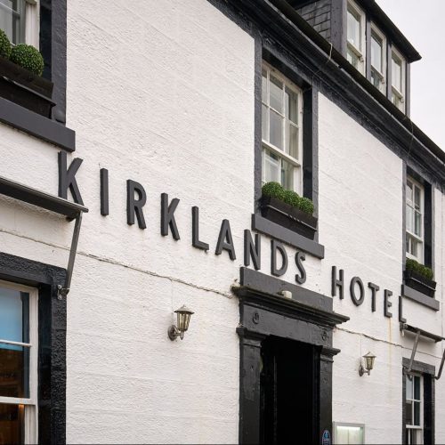 Black lettering sits in the middle of a white hotel building alongside black windows and a black door.