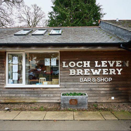 A short wood panelled building with a large window and silver lettering saying Loch Leven Brewery Bar & Shop on the wall in Kinross