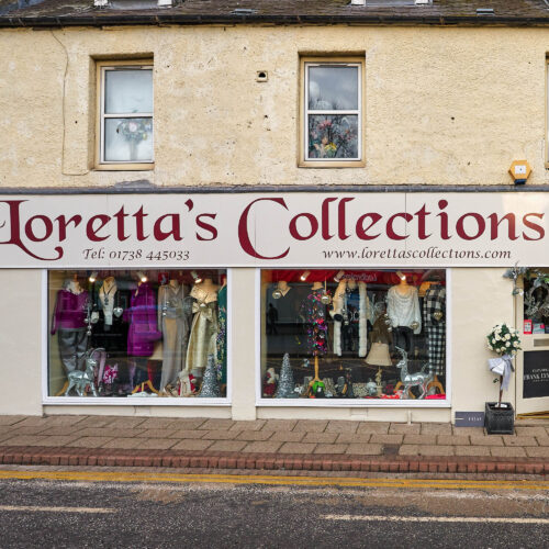 A shop with a large sign written in red cursive font above two large windows displaying mannequins dressed in high end fashion