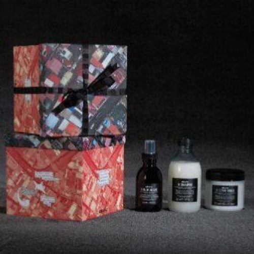 Two decorated red and black boxes tied in ribbon are stacked next to three small containers of creams and lotions