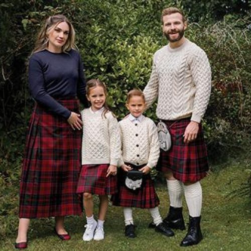 Two young children stand between a man and a woman, all wearing matching red kilts and the man and boy wearing sporrans