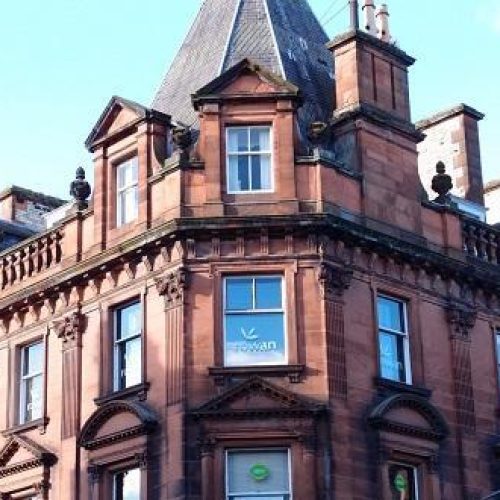 A large red building on the corner of a street in Perth is decorated with ornate red sandstone, a turret roof, and large windows
