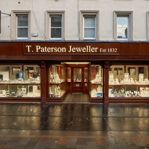 A wood panelled shop in Perth with two large lit up windows displaying a collection of jewellery either side of a wooden door