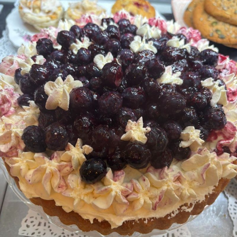 A cake topped with white pipping with pink details and a pile of dark purple glazed berries