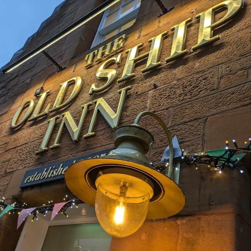 Large gold lettering next to a dimly lit lantern and colourful bunting outside a pub in Perth