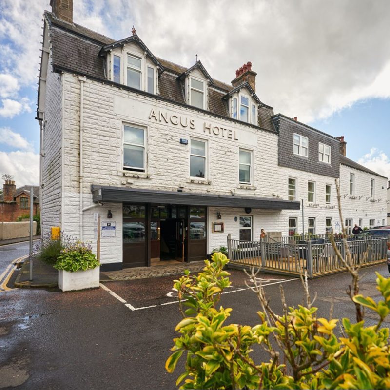 The Angus Hotel and Spa is white brick building with several windows and wooden door standing next to an outside patio