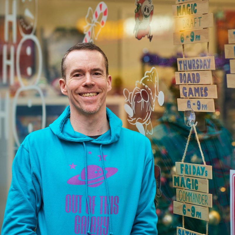 A man wearing a blue patterned jumper stands outside a window decorated with festive pictures and wooden board signs