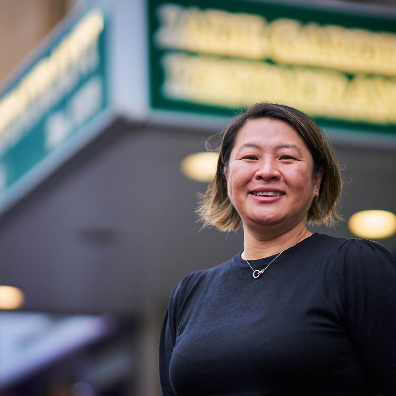 A smiling woman wearing a black shirt and silver necklace stands outside a restaurant in Perth