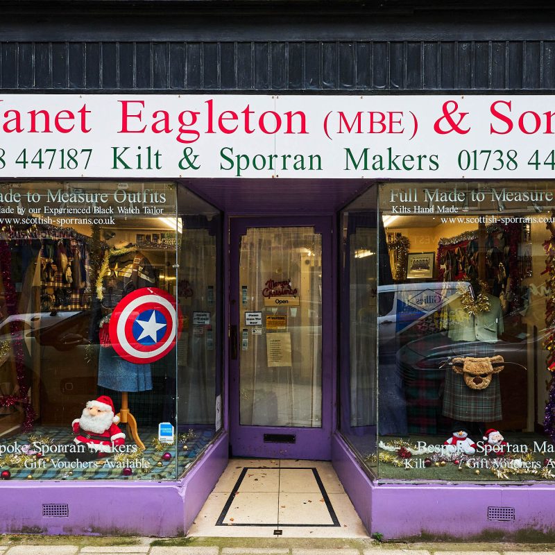 A purple shop with two large windows  display Scottish kilts and costumes, either side of a glass pane door