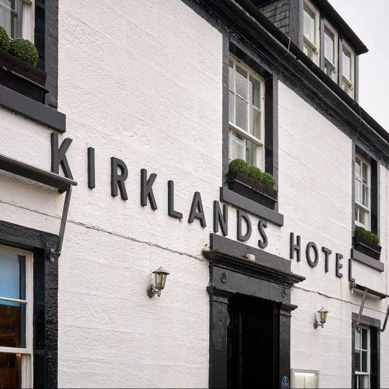 Black lettering sits in the middle of a white hotel building alongside black windows and a black door.