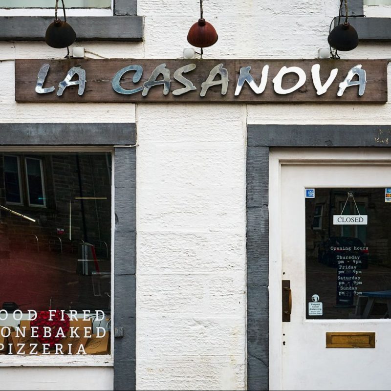 A wooden sign with silver lettering sits above a window and door on a white building