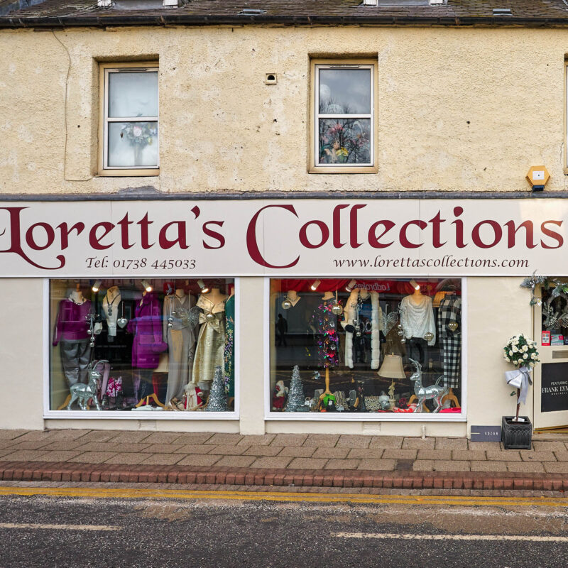 A shop with a large sign written in red cursive font above two large windows displaying mannequins dressed in high end fashion