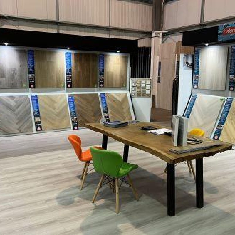A wooden table with two chairs sits in the middle of a room with different wood flooring samples lining the walls