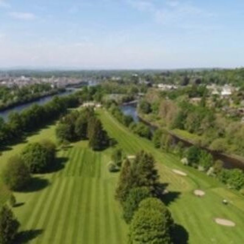 A large open golf course covered in large green trees sitting on an island in the River Tay in Perth