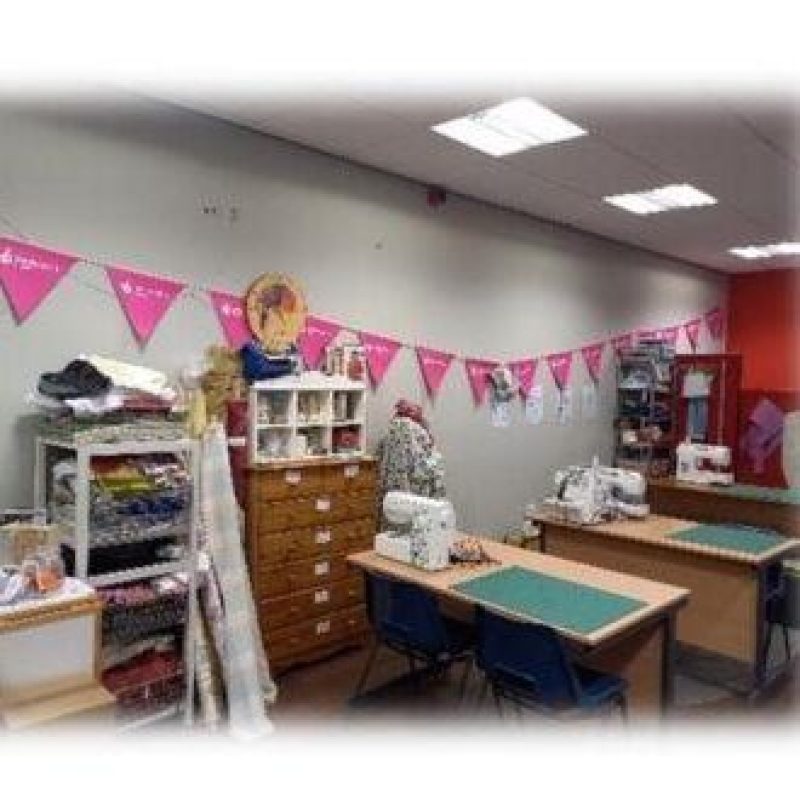 A workshop with two desks holding sewing machines and cutting boards, and large cabinets with sewing supplies lining the wall