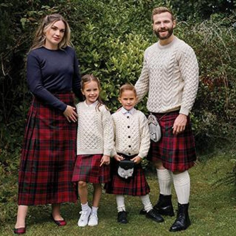 Two young children stand between a man and a woman, all wearing matching red kilts and the man and boy wearing sporrans