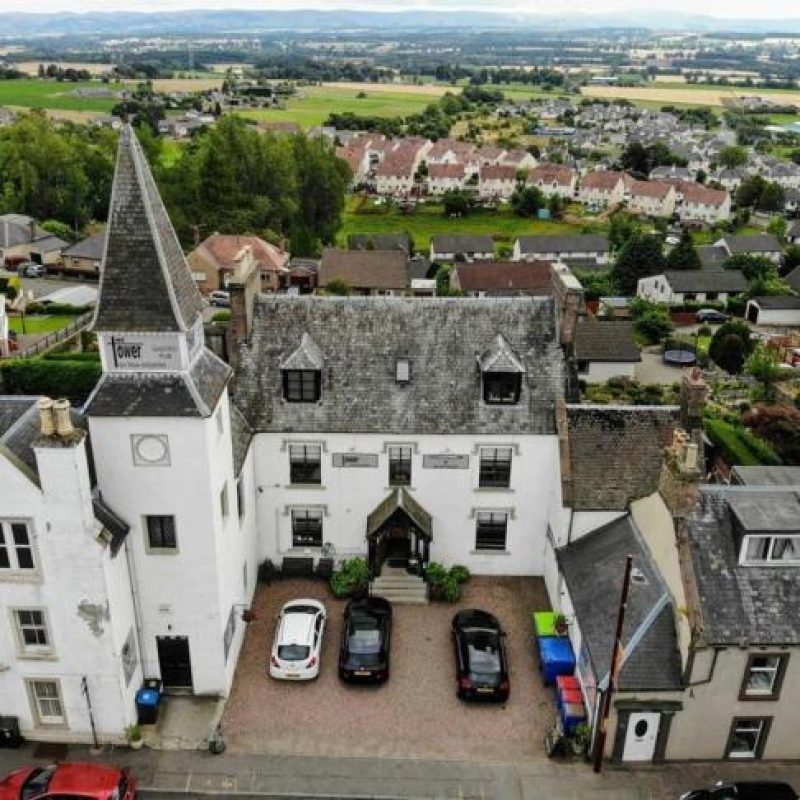 A large white building complete with a turret and large windows sits on a hill overlooking a green landscape