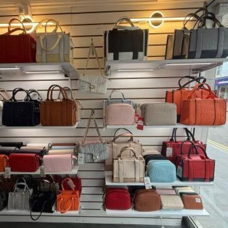 Brightly coloured handbags of varying shapes and sizes sit on white shelves attached to a white shop wall