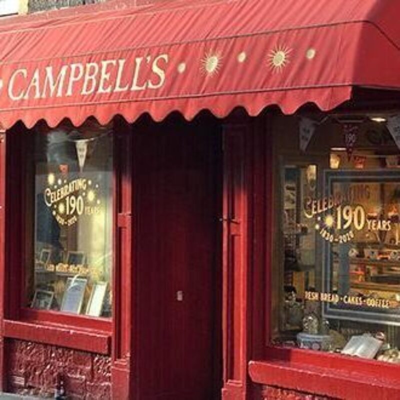 A red shop with a red canopy reading Campbell's in yellow writing has two windows displaying baked goods