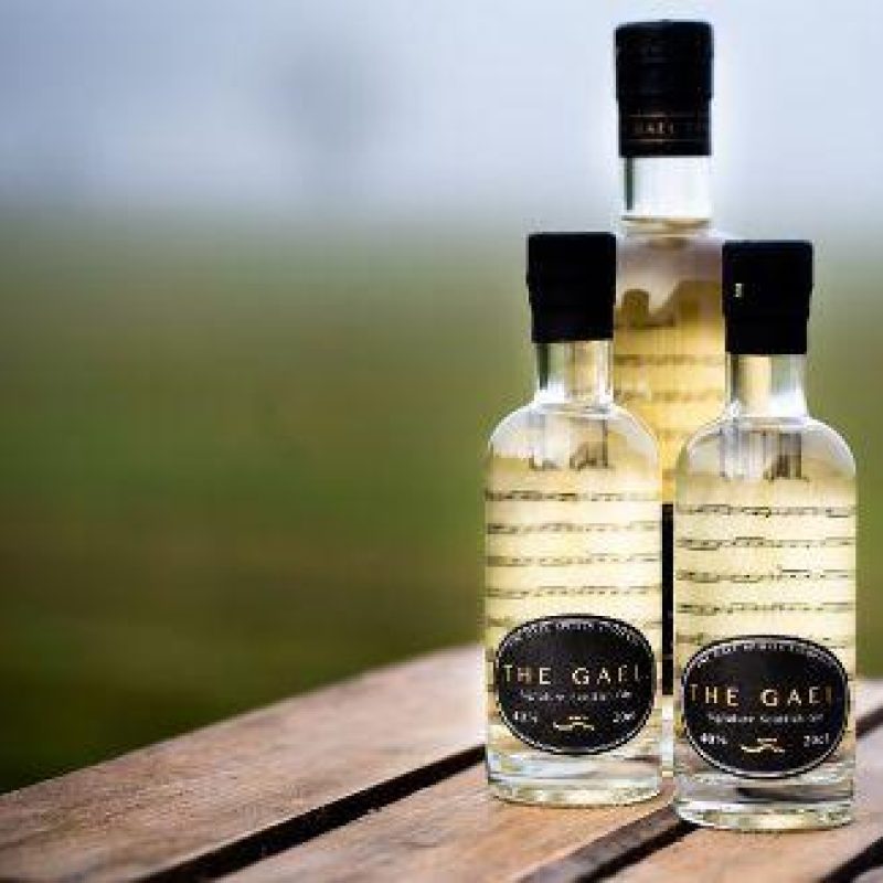 Three glass bottles containing clear liquid are decorated with sheet music lining the inside and a black label on the outside