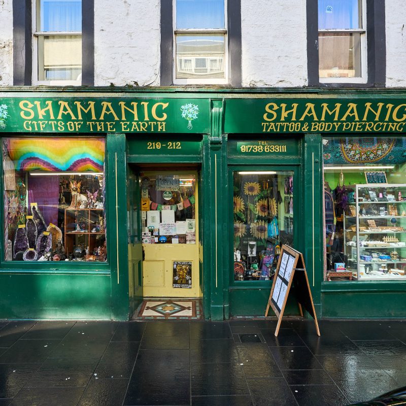 A vibrant green shop with two windows displaying brightly coloured trinkets and jewellery either side of a yellow door