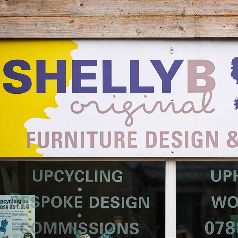 A white and yellow sign with two different purple and pink fonts above a window with white font decals.